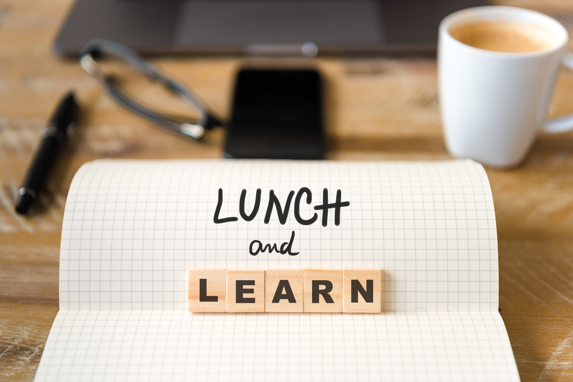 Closeup on notebook over wood table background, focus on wooden blocks with letters making Lunch and Learn text